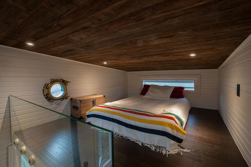 Кровать-чердак имеет стеклянные перила и тонкое окно за кроватью.